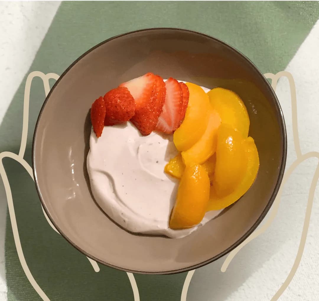 A bowl of Berde's yogurt topped with sliced strawberries and peaches, photographed from above.
