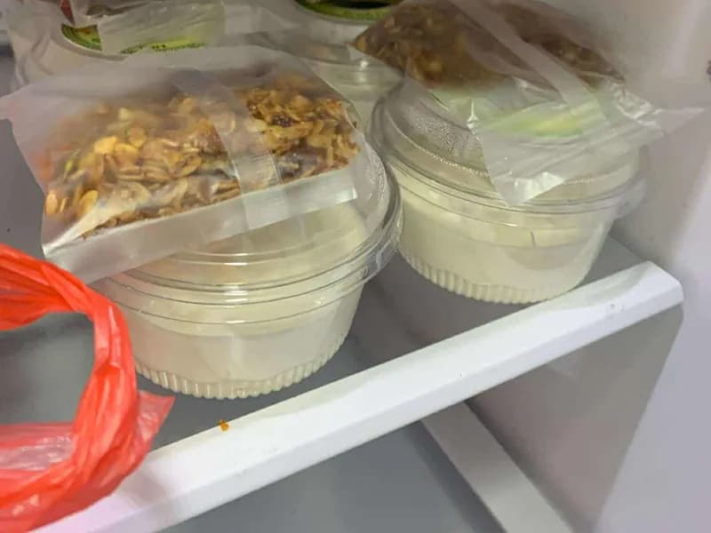 Sealed cups of Berde's yogurt with granola sachets taped to the lids, sitting on a fridge shelf.