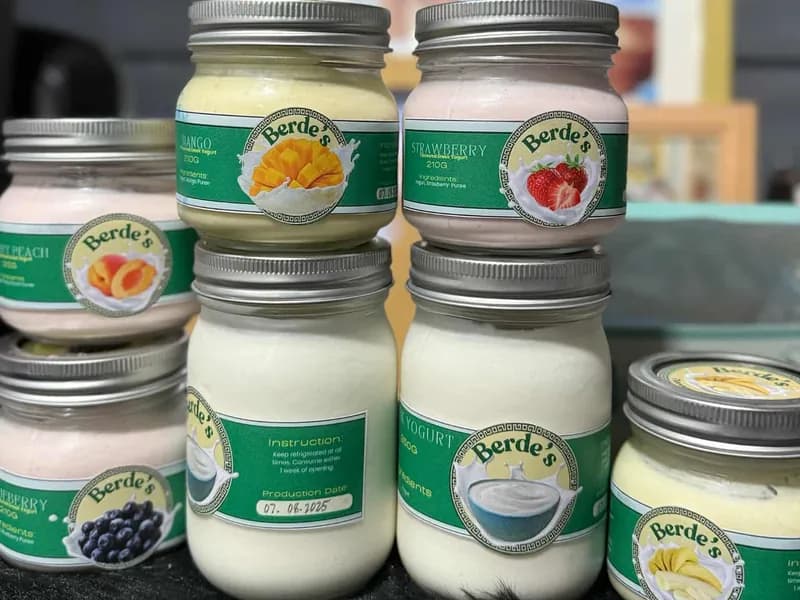 A stack of Berde's jars in Mango, Strawberry, Sweet Peach, Blueberry and Plain, with production dates written on the labels.